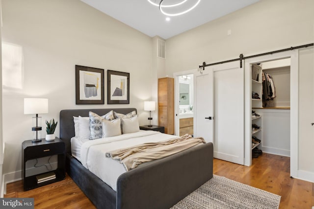 bedroom with ensuite bathroom, hardwood / wood-style flooring, a walk in closet, a barn door, and a closet