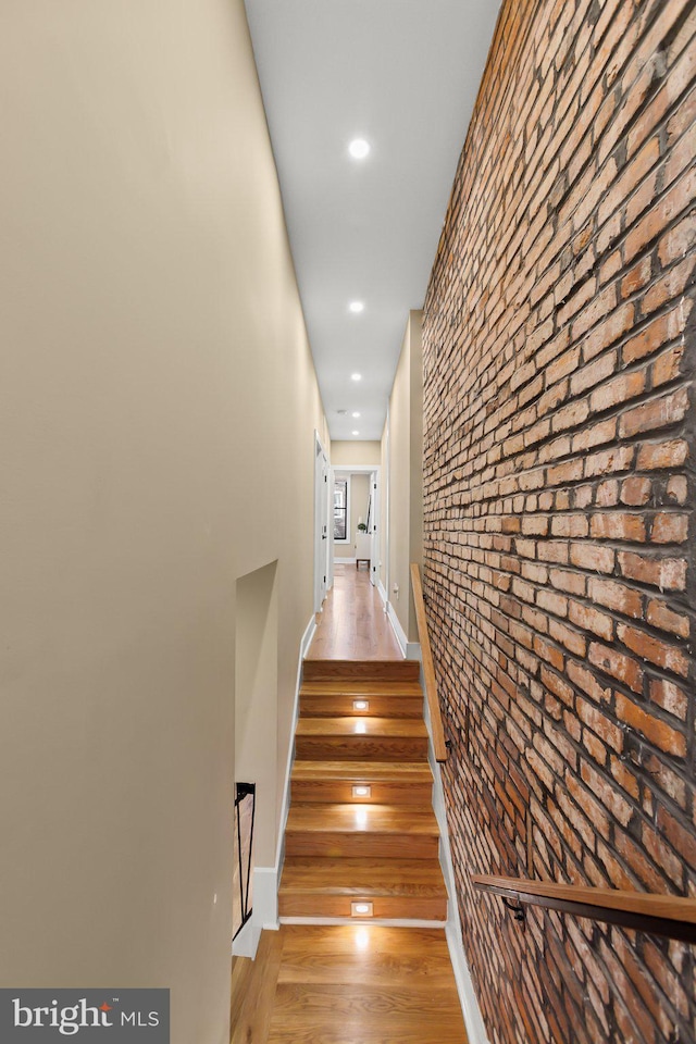 stairway with wood-type flooring and brick wall