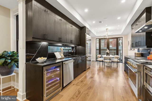 kitchen featuring high quality appliances, beverage cooler, light hardwood / wood-style floors, a raised ceiling, and wall chimney exhaust hood