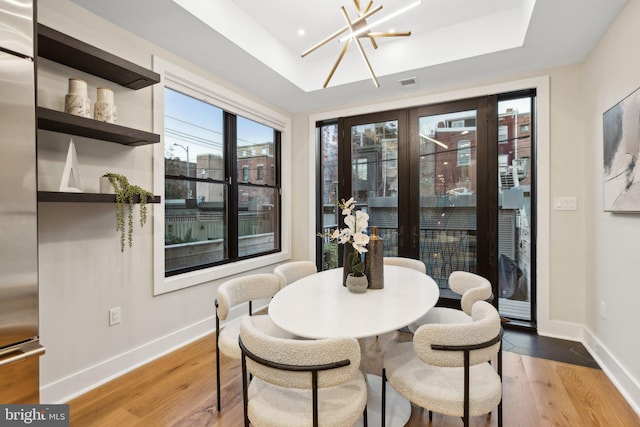 dining area featuring french doors, light hardwood / wood-style flooring, an inviting chandelier, and a tray ceiling