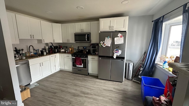 kitchen featuring appliances with stainless steel finishes, sink, white cabinets, decorative backsplash, and light hardwood / wood-style flooring