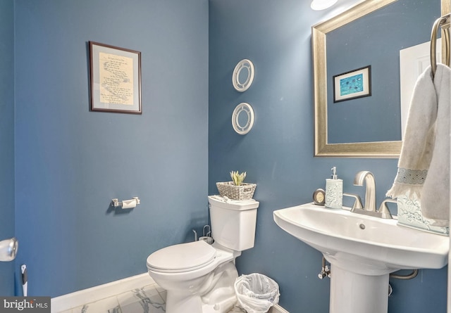 half bathroom with toilet, marble finish floor, and baseboards