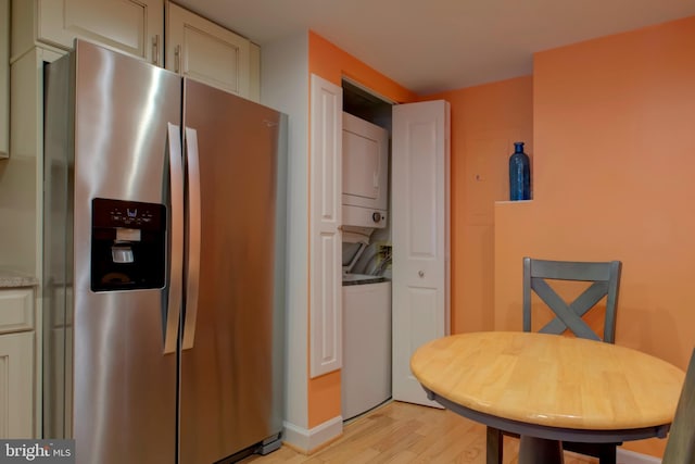 kitchen featuring stacked washer / drying machine, light stone counters, light hardwood / wood-style floors, and stainless steel fridge with ice dispenser