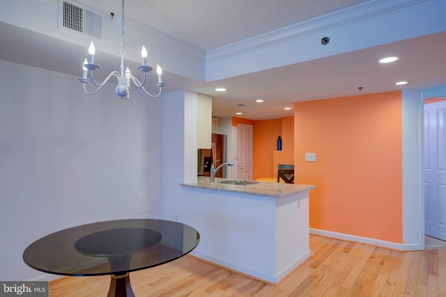 kitchen featuring white cabinets, stainless steel fridge with ice dispenser, decorative light fixtures, kitchen peninsula, and light wood-type flooring