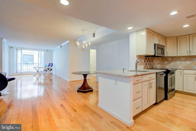 kitchen with sink, appliances with stainless steel finishes, backsplash, hanging light fixtures, and light stone countertops