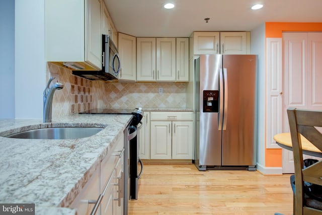 kitchen with sink, light stone counters, stainless steel appliances, light hardwood / wood-style floors, and backsplash