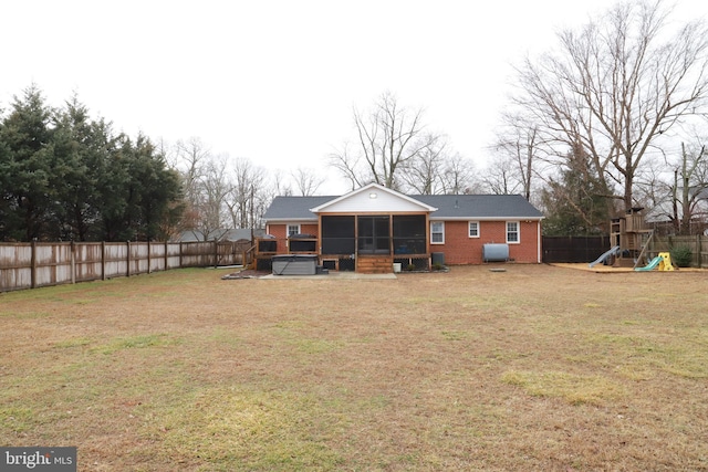 rear view of house featuring a hot tub, a playground, a sunroom, and a lawn