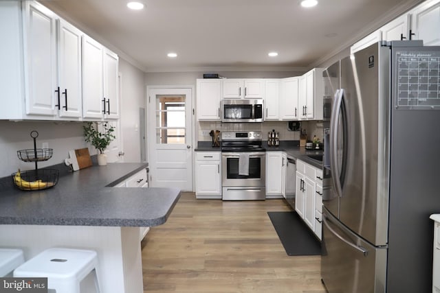 kitchen featuring stainless steel appliances, light hardwood / wood-style floors, ornamental molding, white cabinets, and kitchen peninsula