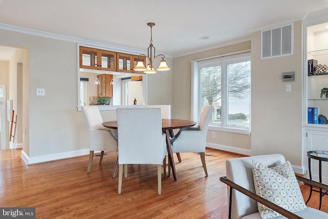 dining room featuring light wood-type flooring, baseboards, visible vents, and ornamental molding