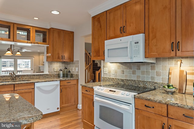 kitchen featuring white appliances, brown cabinetry, a sink, and light stone countertops