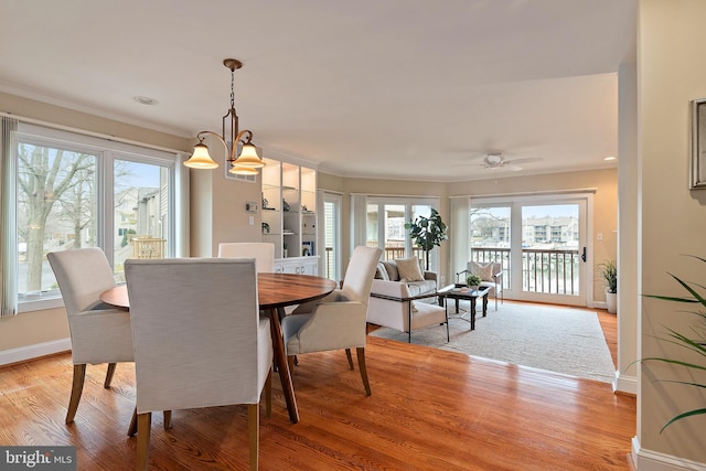 dining space featuring crown molding, ceiling fan with notable chandelier, light wood-style flooring, and baseboards