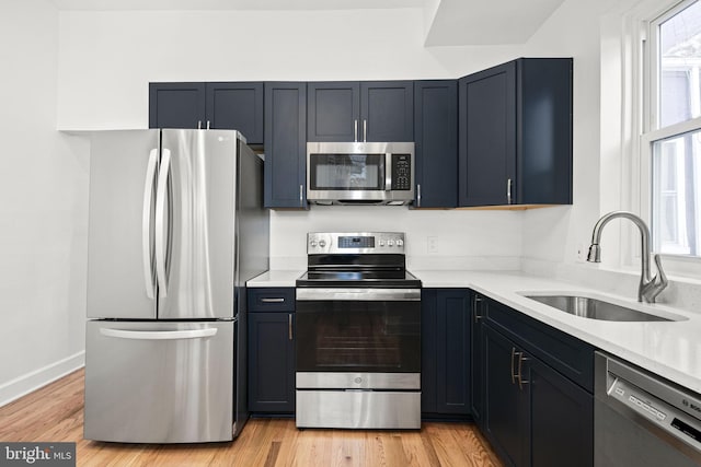 kitchen featuring appliances with stainless steel finishes, sink, light stone counters, and light hardwood / wood-style flooring