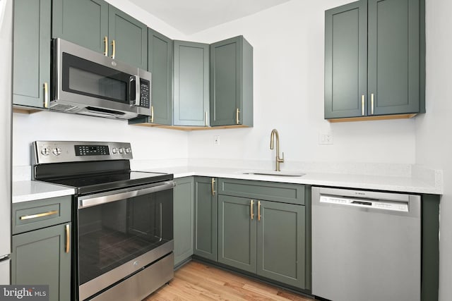 kitchen with sink, stainless steel appliances, light hardwood / wood-style floors, and green cabinetry