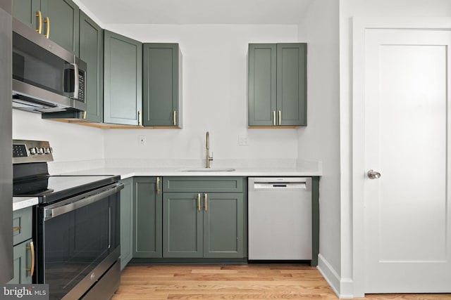 kitchen with green cabinets, appliances with stainless steel finishes, sink, and light wood-type flooring