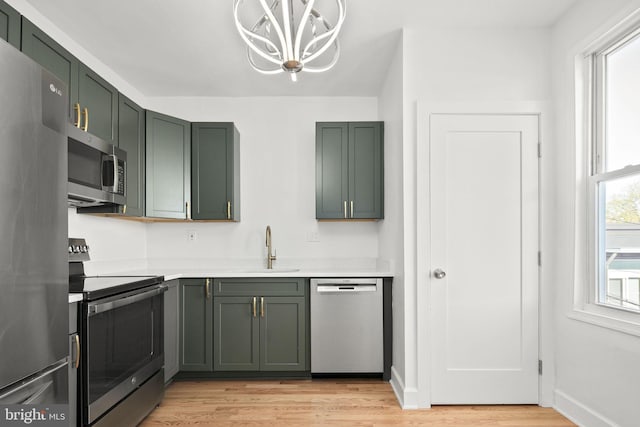 kitchen with sink, stainless steel appliances, green cabinetry, a chandelier, and light wood-type flooring