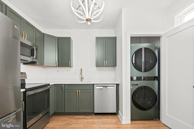 kitchen with sink, stacked washer and dryer, light hardwood / wood-style floors, green cabinetry, and stainless steel appliances