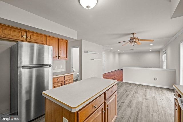 kitchen featuring light hardwood / wood-style flooring, ornamental molding, stainless steel fridge, a kitchen island, and ceiling fan