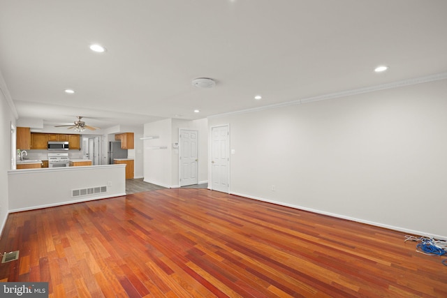 unfurnished living room with crown molding, ceiling fan, sink, and hardwood / wood-style floors