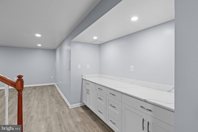 bar featuring white cabinetry, light stone counters, and light hardwood / wood-style floors