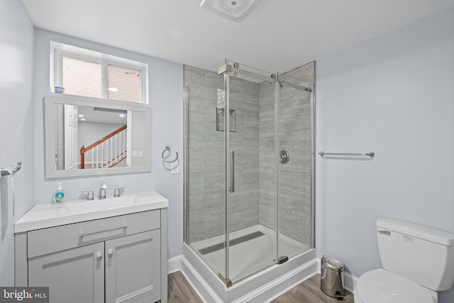 bathroom featuring wood-type flooring, toilet, a shower with door, and vanity