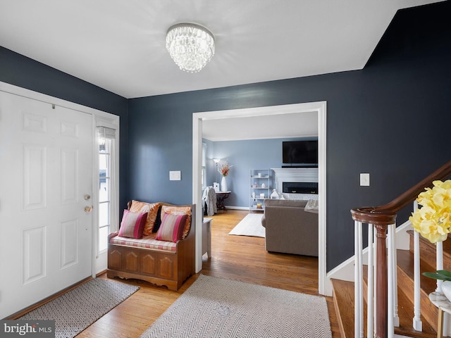 entryway with a notable chandelier, a fireplace, wood finished floors, baseboards, and stairway