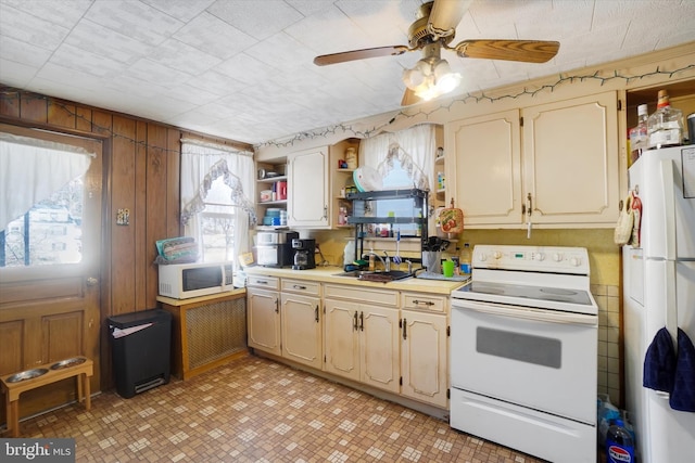 kitchen featuring sink, white appliances, ceiling fan, and wood walls