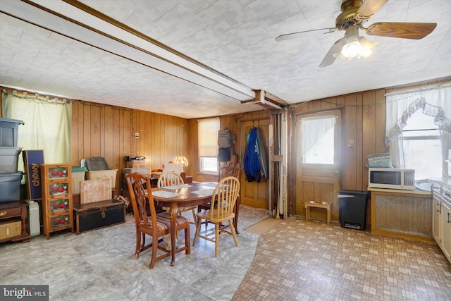 dining area with ceiling fan and wood walls