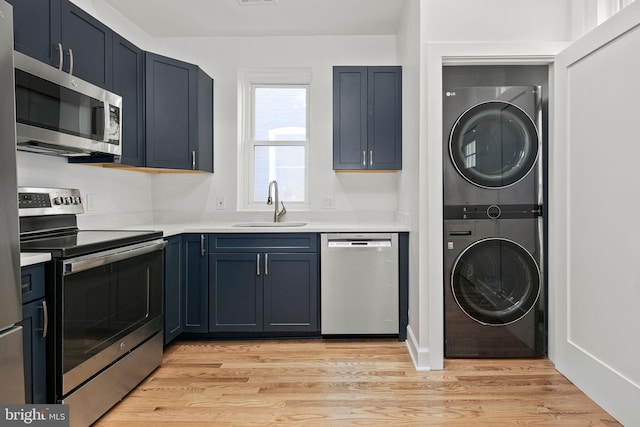 kitchen with appliances with stainless steel finishes, blue cabinets, sink, stacked washer and clothes dryer, and light hardwood / wood-style floors