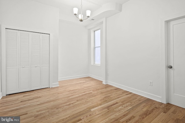 unfurnished bedroom featuring an inviting chandelier, light hardwood / wood-style floors, and a closet