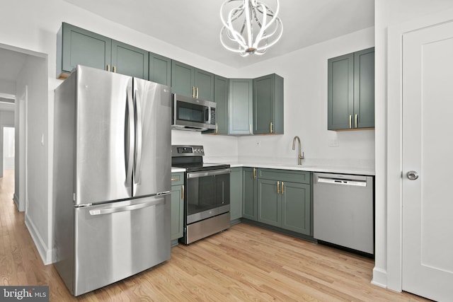 kitchen featuring sink, hanging light fixtures, green cabinetry, stainless steel appliances, and light hardwood / wood-style flooring