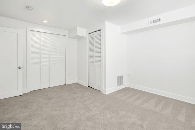 unfurnished bedroom featuring light carpet and multiple closets