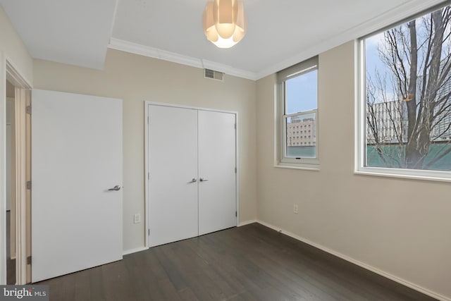 unfurnished bedroom with dark wood-type flooring, ornamental molding, and a closet