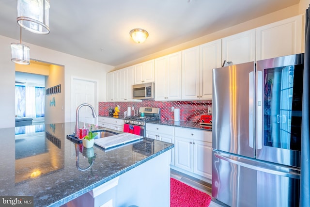 kitchen featuring sink, appliances with stainless steel finishes, white cabinetry, hanging light fixtures, and dark stone counters