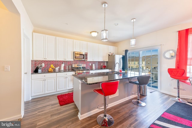 kitchen with pendant lighting, white cabinetry, stainless steel appliances, a kitchen breakfast bar, and tasteful backsplash