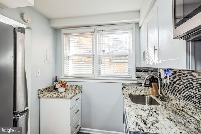 kitchen with stainless steel appliances, white cabinetry, sink, and light stone counters