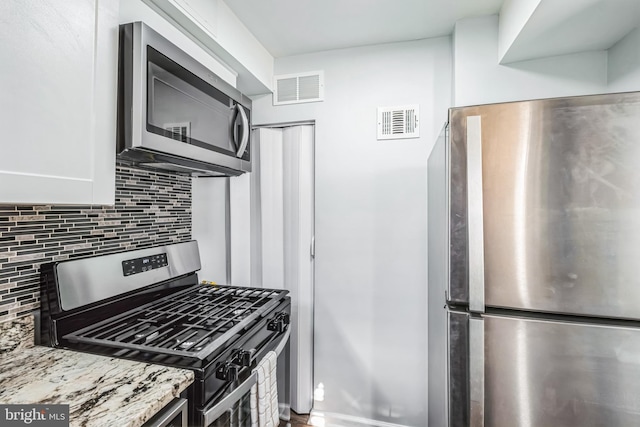 kitchen with light stone counters, backsplash, white cabinetry, and appliances with stainless steel finishes