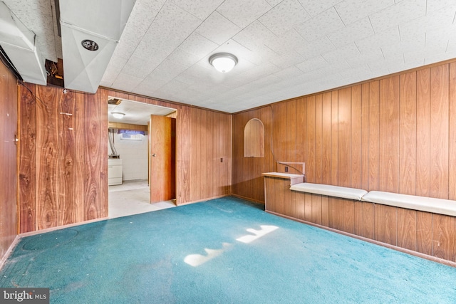 unfurnished room with washer / clothes dryer, wooden walls, and light colored carpet