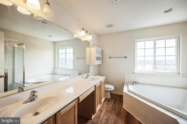 bathroom with double vanity, a garden tub, a sink, and wood finished floors