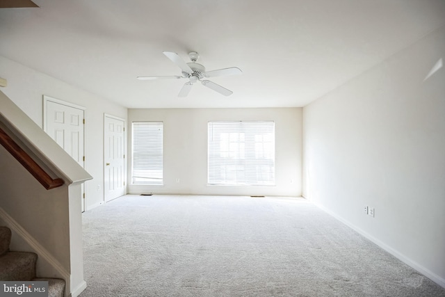 spare room featuring carpet floors, ceiling fan, stairs, and baseboards