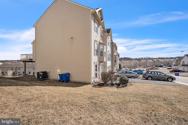 view of side of home featuring a lawn, a residential view, and central air condition unit