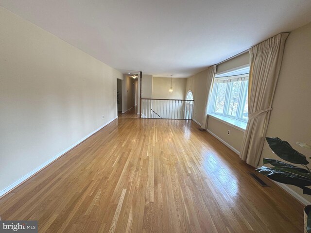 empty room with light wood finished floors, visible vents, and baseboards