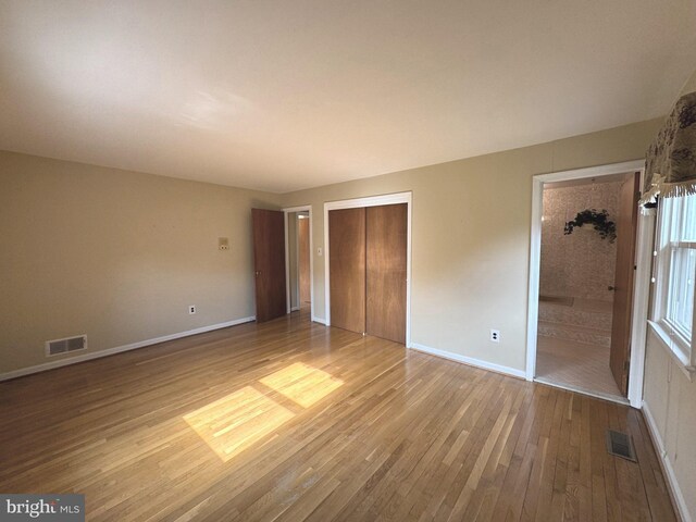 unfurnished bedroom featuring baseboards, connected bathroom, visible vents, and light wood-style floors