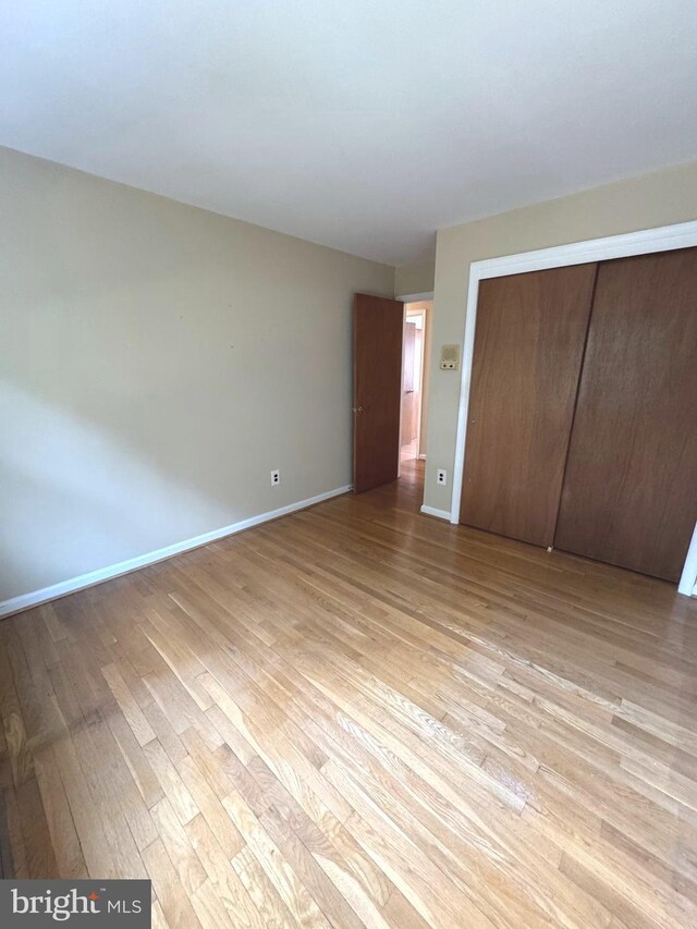 unfurnished bedroom with light wood-type flooring, baseboards, and a closet