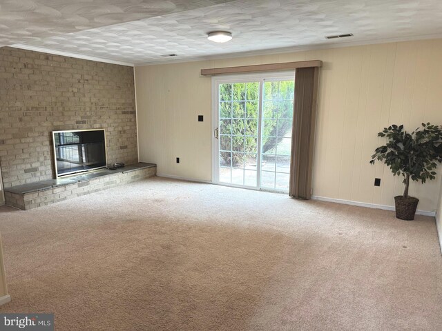 unfurnished living room with a brick fireplace, carpet flooring, crown molding, and visible vents