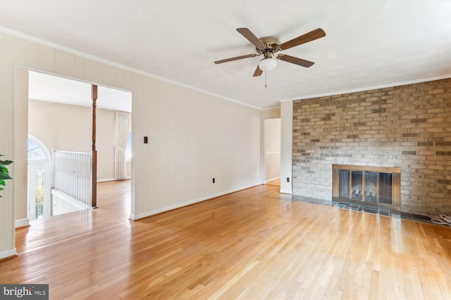 unfurnished living room featuring light wood-style floors, a brick fireplace, ornamental molding, and ceiling fan