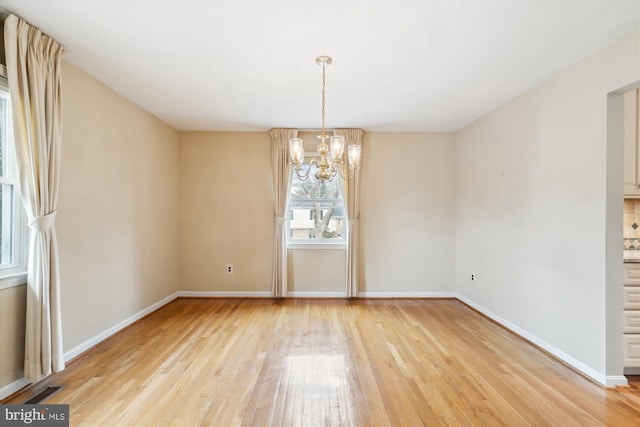 unfurnished dining area featuring visible vents, light wood-style flooring, baseboards, and an inviting chandelier