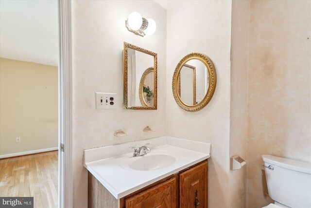 half bathroom with vanity, toilet, and wood finished floors