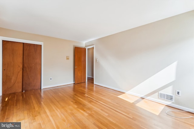 unfurnished bedroom featuring baseboards, a closet, visible vents, and wood finished floors