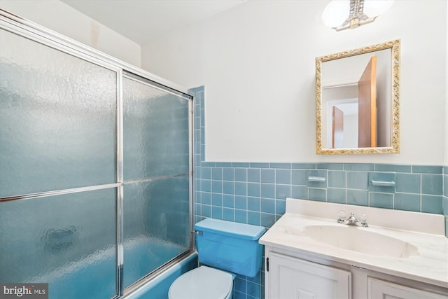 full bath with toilet, a wainscoted wall, bath / shower combo with glass door, vanity, and tile walls