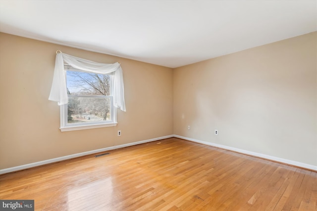 empty room with light wood-style flooring, visible vents, and baseboards